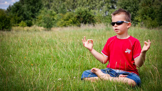Eleven Fears and Misconceptions About Meditation young boy wearing sunglasses meditating in an open field